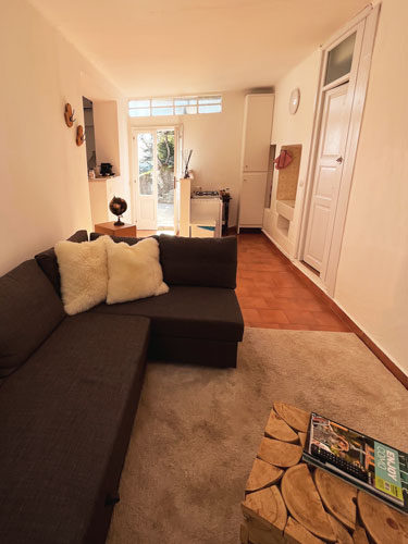 The living room of the Nano Guesthouse: a long sofa, a coffee table, decorations, a door in the background and the garden outside.